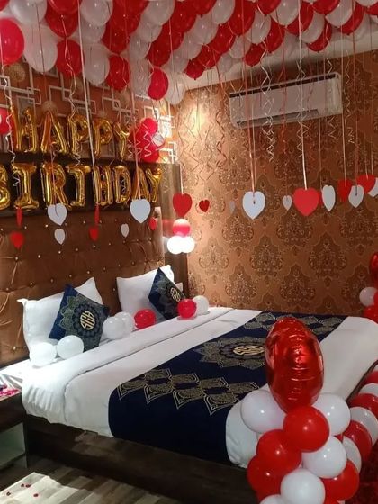 A classic romantic bedroom decoration in red and white. The setup includes balloons on the ceiling, heart-shaped cutouts, and a decorated bed.
