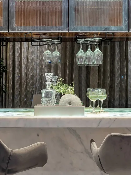 The perfect setup for an evening drink. This bar features a marble countertop, elegant glassware, and a crystal decanter, all beautifully illuminated against a textured backdrop.