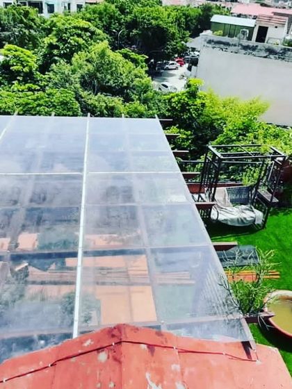 A top-down view showing the installation of a polycarbonate sheet roof over a pergola, providing protection from rain while still allowing natural light to pass through.