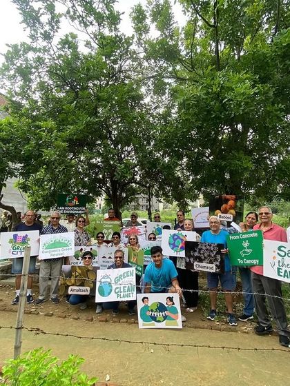 The DLF Senior Citizen Council proudly holds up signs after planting 150 saplings at Aravali Creek, showcasing their unwavering commitment to the environment.