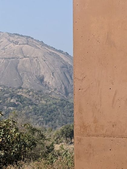 A view of the Savanadurga monolith framed between two earthen walls at the Unnathi Farm project. The architecture is designed to connect with its powerful landscape.
