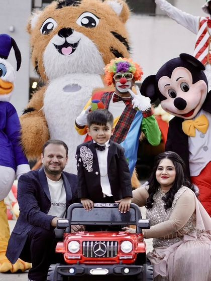 A fun group photo with multiple character mascots, including Mickey Mouse, Donald Duck, and a tiger, at Neel's carnival party.