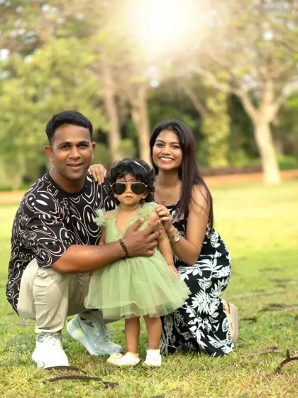 A fun family photo where the little girl sports cool sunglasses, posing with her parents in a sunny park.