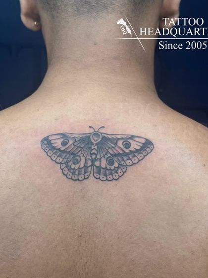 A detailed moth tattoo on the upper back, symbolizing transformation and attraction to light.