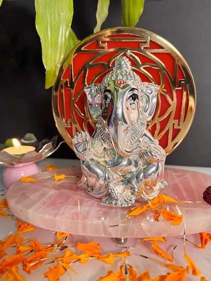 This composition shows the Ganesha on a rose quartz base with a lit diya, creating a warm and inviting spiritual atmosphere.