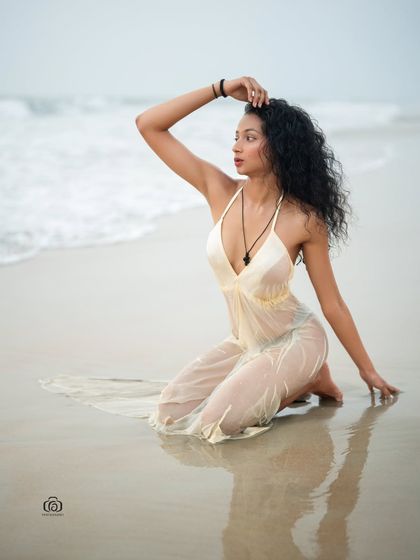 A kneeling pose on the wet sand, with the sheer white dress spread out. The reflection in the sand and the soft light create a dreamy and romantic beach portrait.