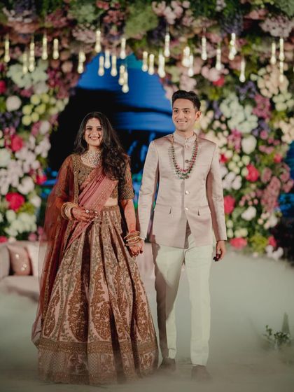 The grand entrance. The couple walks in hand-in-hand at their reception, surrounded by theatrical smoke. Their coordinated outfits look stunning against the floral backdrop, creating a truly cinematic moment.