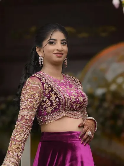 A portrait of a client in a rich magenta velvet lehenga. The crop top features intricate gold Zardozi work on the bodice and sheer sleeves, combining a traditional craft with a modern silhouette.