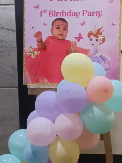 This custom welcome board was created for a butterfly and fairy-themed first birthday. It features a picture of the birthday girl and is surrounded by pastel balloons to match the party's color scheme.