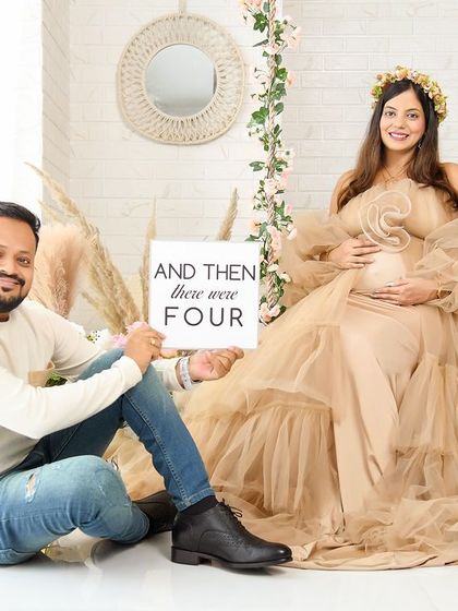 A fun and sweet family announcement photo. The couple is in our boho swing set, holding a sign that says "And then there were four," celebrating their growing family.