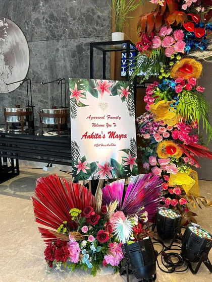 A personalized welcome sign for a Mayra ceremony, part of a vibrant carnival-themed decor. The sign is surrounded by colorful floral arrangements that match the energy of the event.