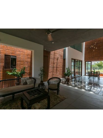 The semi-open living area in 'An Earthy Affair' is defined by exposed brick and a dark ceiling, creating a cozy yet spacious feel. Light filters through the space, highlighting the rich textures of the materials.