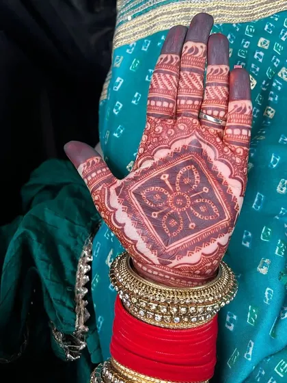 The beautiful dark stain on a happy client's hand, perfectly complemented by her traditional red and gold bangles.
