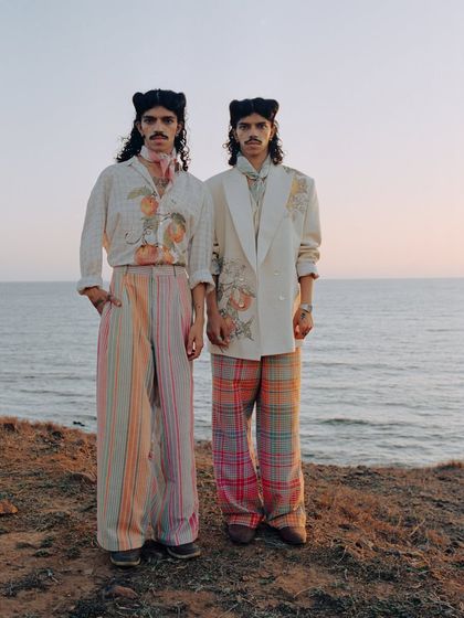 A full-length shot of two models for a menswear editorial set on the coast. The styling mixes prints and soft tailoring, creating a cohesive story that feels both romantic and modern. This is a key image from the series.