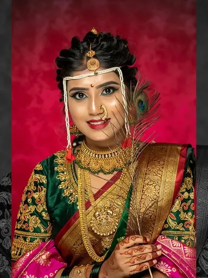 A Maharashtrian bride holding a peacock feather, a symbol of grace. The makeup features a classic winged liner and a pop of colour on the lips to complement the green saree.