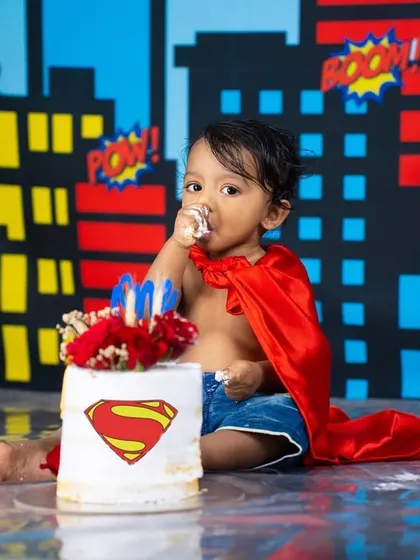 Even superheroes need a cake break. This little Superman is enjoying his first birthday cake against a fun, comic-book city skyline.
