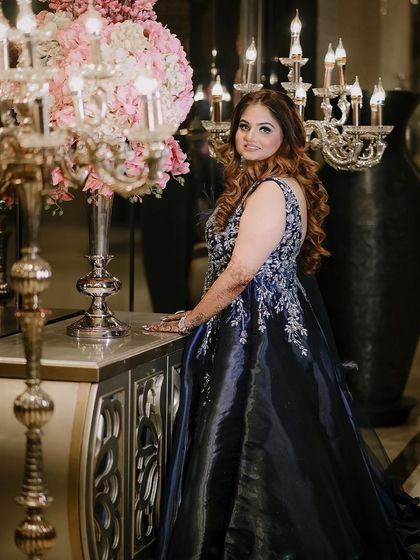 An elegant portrait of the bride standing next to a grand floral arrangement and candelabra.