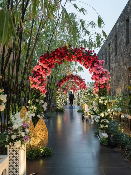 A stunning floral archway of red and pink roses creates a romantic pathway for guests. This is an example of how we use decor to guide the guest experience and build anticipation.