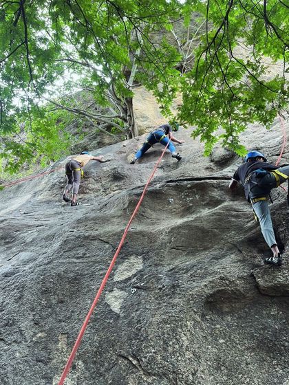 Multiple climbers practice their top-roping skills simultaneously on a rock face in Ramanagara. This setup allows for maximum practice time under the watchful eyes of our instructors.