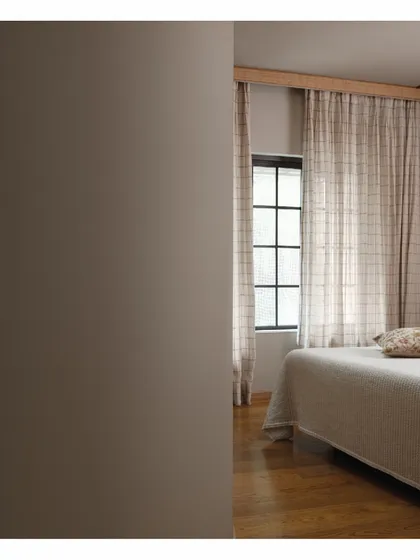 A glimpse into the master bedroom, a warm space defined by its desert tones. Taupe walls and buttery sand-colored sheers soften the light, while the honey and walnut dual-toned flooring adds richness. It's a room designed to be a dusky and cozy retreat.