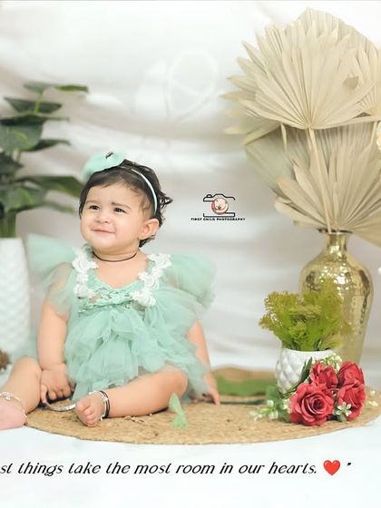 An adorable baby girl sits happily in a beautifully styled boho studio setup. The soft lighting and arrangement of dried florals, pampas grass, and rustic props create a dreamy atmosphere for this portrait.