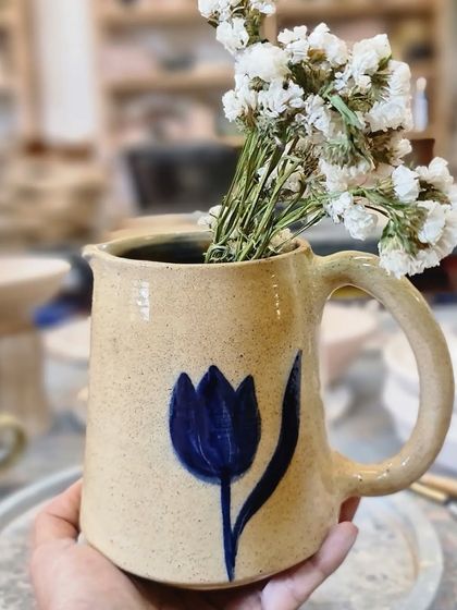 Holding the blue tulip jug. The speckled stoneware clay gives it a rustic charm that contrasts beautifully with the simple, elegant painting.