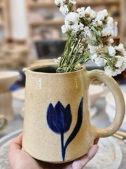 Holding the blue tulip jug. The speckled stoneware clay gives it a rustic charm that contrasts beautifully with the simple, elegant painting.