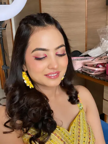 A stunning Haldi look with a pop of color on the eyes. The pink eyeshadow and fresh, dewy skin perfectly complement the yellow outfit and floral earrings.