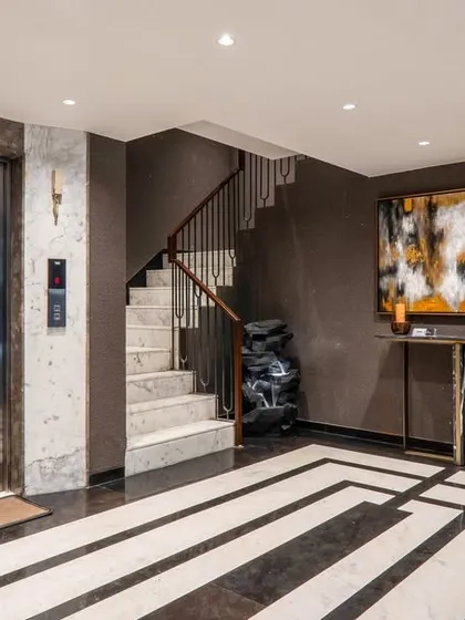 The lift lobby in the same project uses a dark, textured wallpaper and a bold geometric pattern on the floor. A large piece of abstract art adds a pop of color and personality.