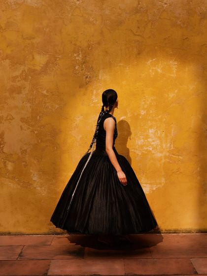 A model in a voluminous black dress against a striking yellow wall, playing with light and shadow.