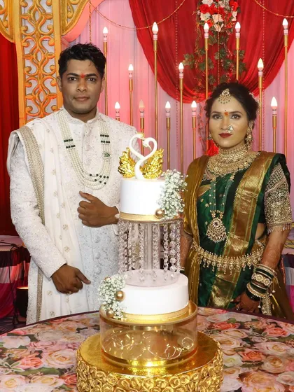 A full view of the couple and their elegant swan-themed engagement cake. The gold and white design with delicate floral touches perfectly complements their traditional outfits.