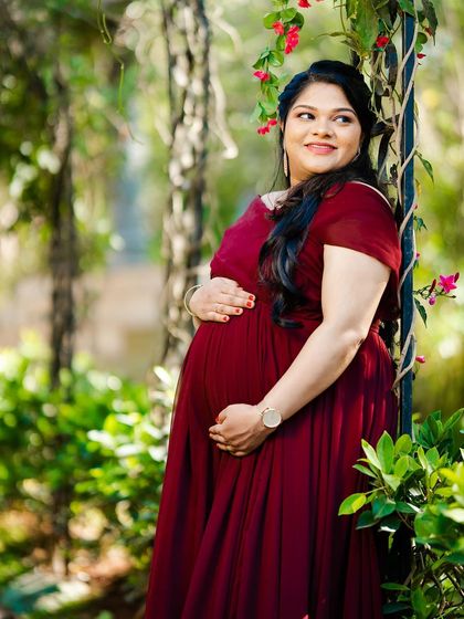 A classic and elegant solo maternity pose. The simple, solid-colored red gown beautifully accentuates the baby bump, while the garden provides a soft, natural background.