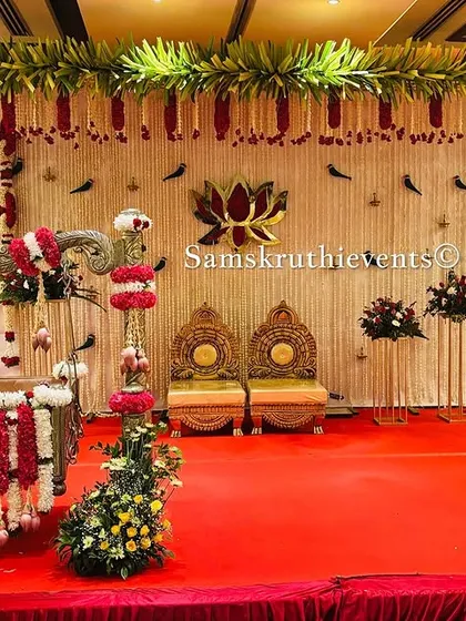 A complete stage setup for a naming ceremony. It features a decorated cradle, seating for the parents, and a backdrop of hanging jasmine strings with a central lotus motif.