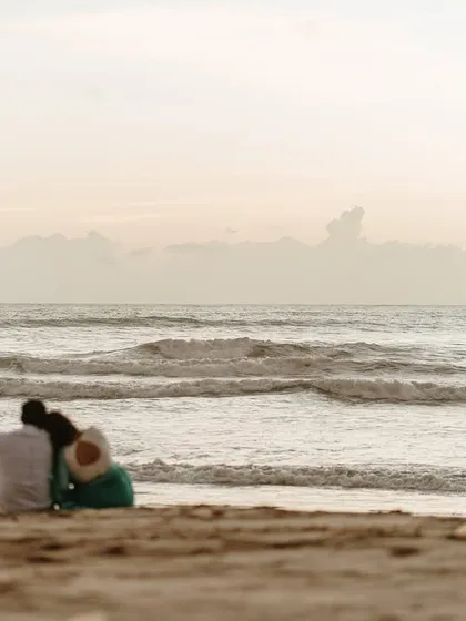 A quiet, intimate moment of the couple sitting together on the sand, looking out at the ocean and dreaming of their future.