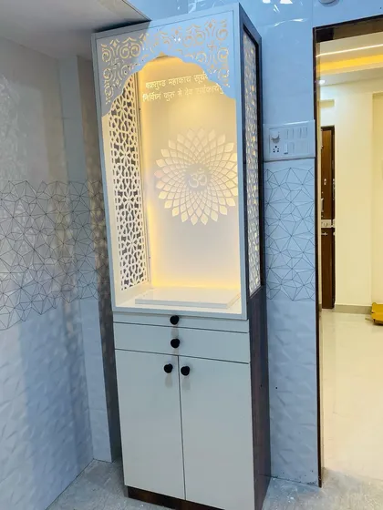 A modern mandir in a white and dark wood finish. The intricate jaali work on the sides and the backlit 'Om' create a peaceful and elegant prayer corner.