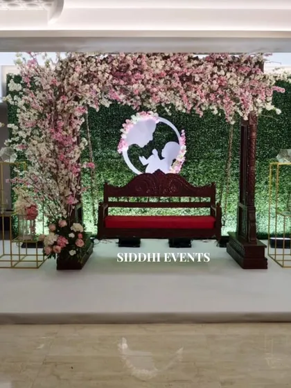 Celebrating new beginnings with this enchanting baby shower decor. A classic wooden swing, adorned with a canopy of delicate pink cherry blossoms against a green hedge wall, creates a beautiful and serene setting for the mother-to-be.