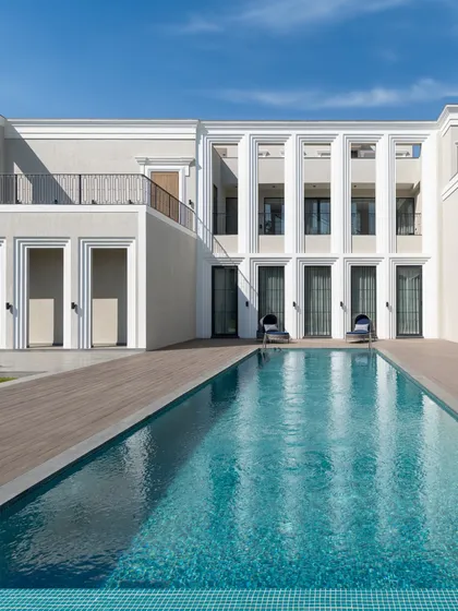 The clean geometry of this modern-classical facade is softened by the tranquil blue of the swimming pool. We design homes as complete experiences, where every exterior view is composed with artistic intent.