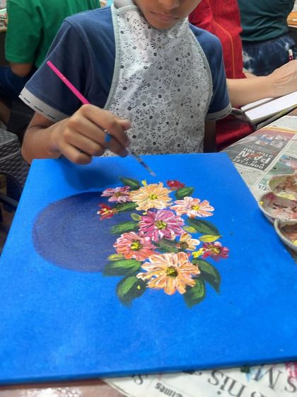 A student in our kids' canvas painting course adding the final touches to his floral artwork. He is learning how to layer colors to create depth and dimension in the petals.