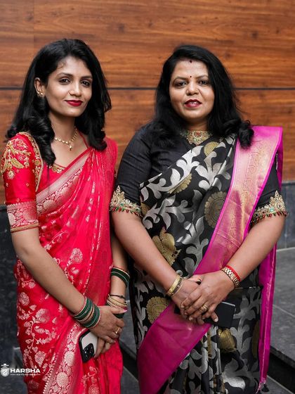 Two of our gorgeous clients, one in a vibrant red Banarasi and the other in a black and pink floral brocade, both radiating elegance.