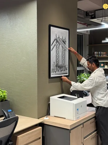 The final touches. A craftsman carefully hangs a piece of art in a newly completed corporate office. This step is crucial, as art is what makes a space feel truly human and complete.