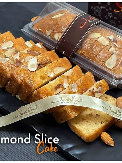 A perfect slice of happiness, our Almond Slice Cake is a testament to simple elegance. This image displays a beautifully baked loaf, generously topped and filled with almond slivers, pre-sliced for easy sharing and enjoyment.