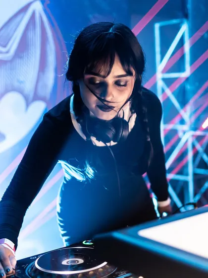 A close-up of me as Wednesday Addams, focused on the mix. I pay attention to every detail, from the music to the look, to create a complete thematic experience.