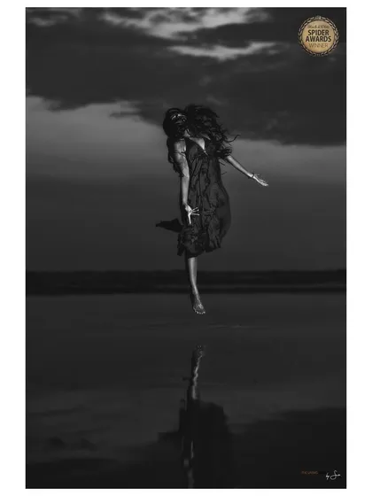 This image, which received an Honourable Mention at the Black & White Spider Awards, is called 'The Blessing'. It explores a sense of freedom and connection to the elements, capturing a moment of pure, weightless expression against the evening sky.