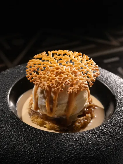 A scoop of vanilla ice cream with a caramel drizzle and a delicate sugar tuile. The dark, moody lighting makes this dessert feel luxurious.