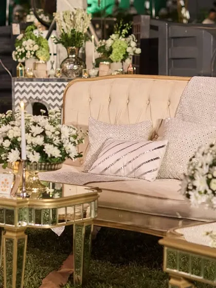 A lounge area with vintage-style cream sofas and mirrored tables. The space is filled with bouquets of white chrysanthemums, creating a serene and royal atmosphere.