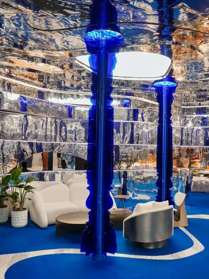 Two glowing cobalt columns anchor the space, their traditional form reimagined in a futuristic material. They act as sculptural elements that draw the eye and bathe the installation in a vibrant blue light, enhancing the immersive quality of the design.