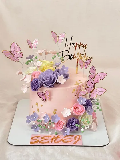 A beautiful birthday cake for Sehej, adorned with a garden of pastel flowers and fluttering butterflies. The delicate colors and gold accents create a soft, dreamy look.