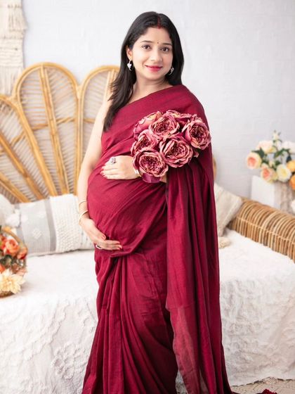 A portrait that blends tradition with modern studio photography. The mother-to-be looks elegant and serene holding a bouquet while dressed in a deep red saree.