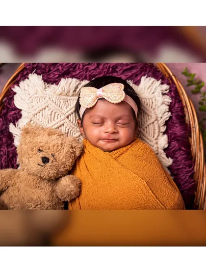 A detailed close-up of a newborn's sweet, sleeping face. The baby is nestled with a teddy bear, and the soft focus on the foreground creates a dreamy and intimate feel.
