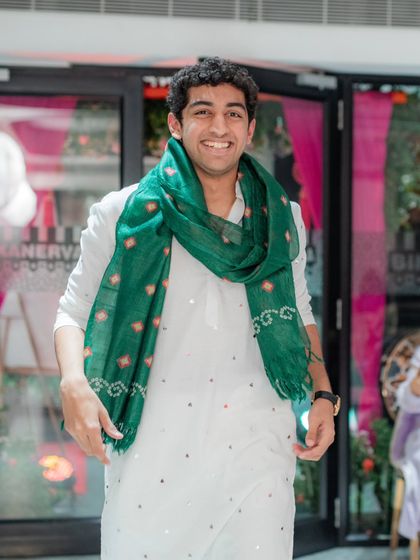 A candid shot of a family member looking happy and relaxed at a pre-wedding event. The simple white kurta is elevated by a green bandhani scarf, a simple styling trick that adds a lot of impact.